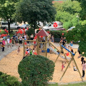 Kinder und Erwachsene mit roten Luftballons weihen einen Spielplatz ein