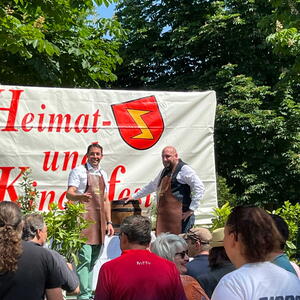 Wolfgang Gogel steht mit Schürze auf einer Bühne und sticht das Fass an